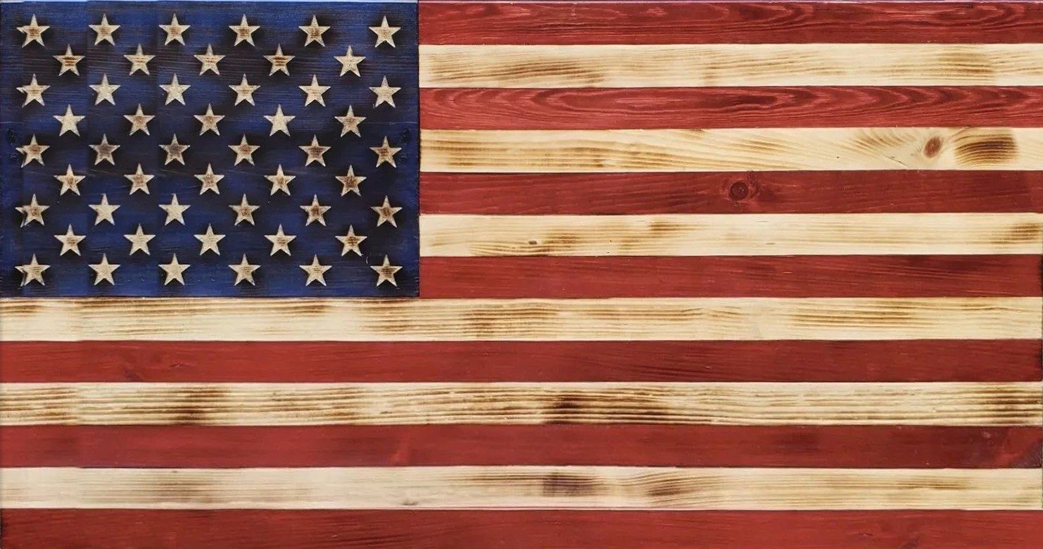 Torched wooden American flag with red and natural stripes and carved stars on a blue field