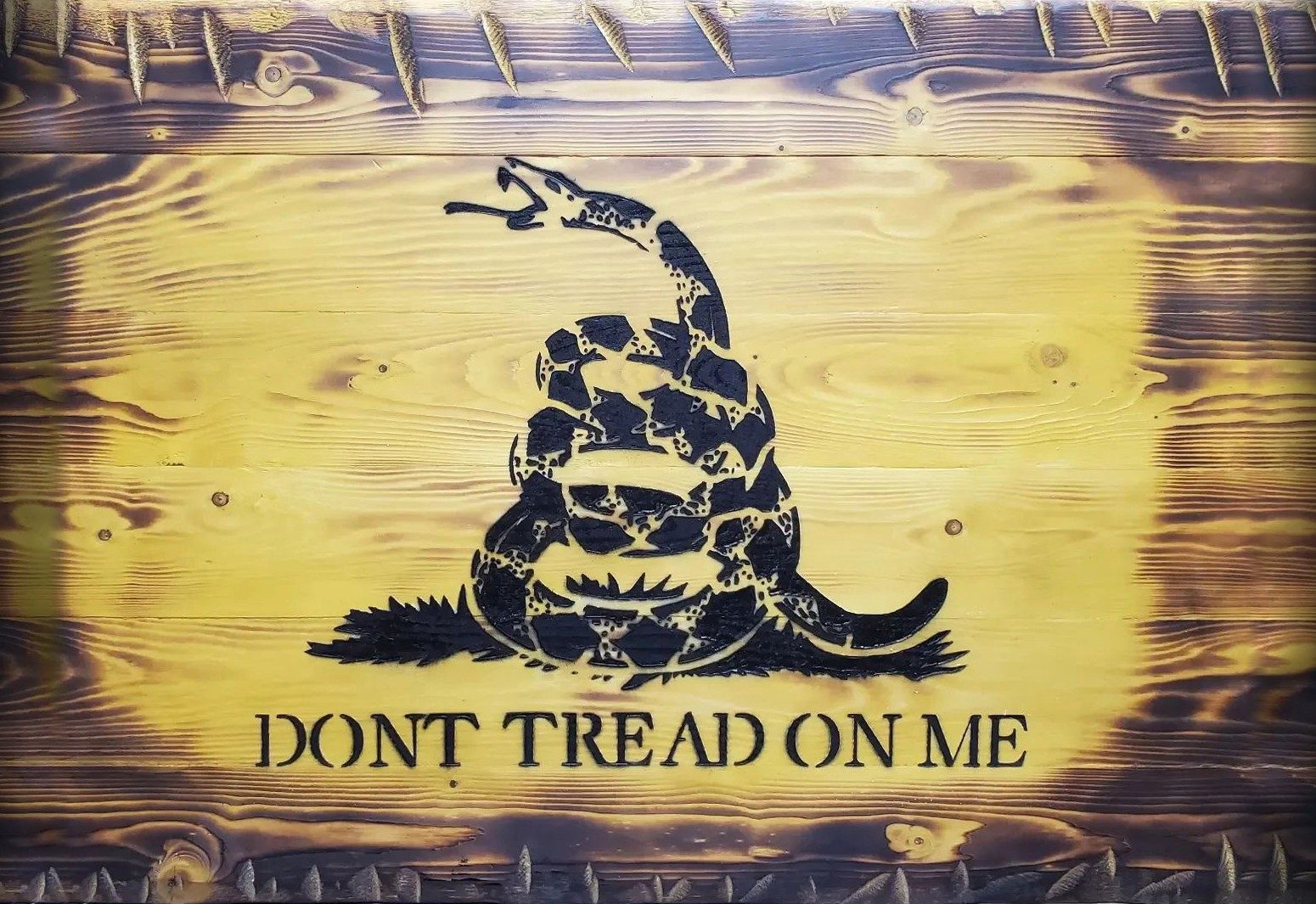 Torched yellow wood sign with a carved coiled snake and the words Dont Tread On Me